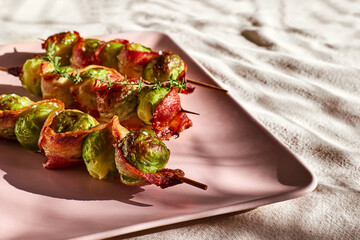 Skewers with Brussels sprout wrapped in bacon, grilled and served on pink plate.