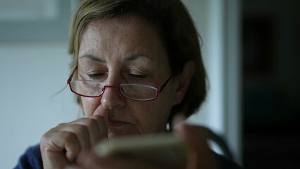 Older lady scratches nose and face while reading content online with the use of smartphone device....
