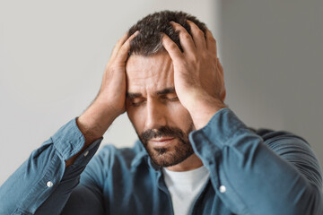 man struggles with headache pain holding head in hands indoors - obrazy, fototapety, plakaty