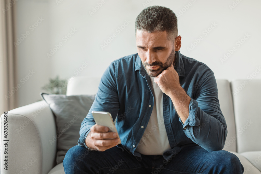Poster thoughtful middle aged man doom scrolls through phone at home