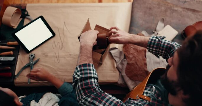 Box, team and people packing for delivery, shipping and ecommerce in leather workshop top view. Package, boxes and stock in small business for logistics, distribution of order and tablet mockup space