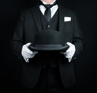 Portrait of Butler in Dark Formal Suit and White Gloves Holding a Bowler Hat. Concept of Service Industry and Professional Courtesy.