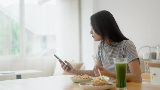 Happy asian woman using mobile phone during breakfast&nbsp;or eating lunch while working from home .