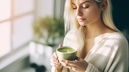 Poster Blonde caucasian beauty young woman drinking tea matcha. Natural light © yevgeniya131988