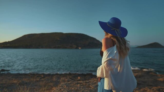 Woman in a blue hat at sunset by the sea.