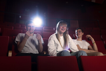 Three friends in the cinema hall, a girl and two boys having fun watching a film in the empty movie...