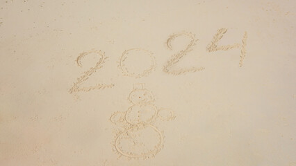 sandman snowman and new 2024 year inscription written on the sand. Happy winter holidays. Merry Christmas and happy tropical new year. Celebrate holiday on the beach.