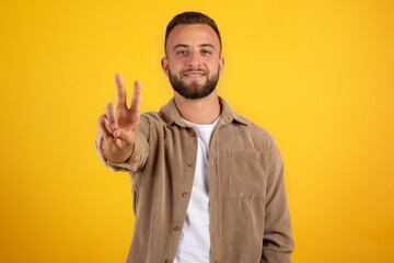 Smiling millennial european guy with beard in casual make peace hand sign, show two fingers