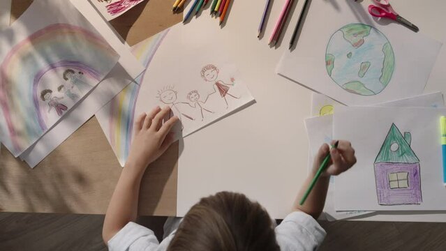 Boy at desk, skillfully painting picture of his family and vibrant rainbow. Drawing reflects happiness and love present in harmonious family. Heartwarming image of his family, dream about happiness