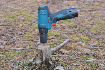 one colored screwdriver electric drill sticks on a gray stump on the street