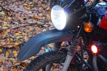 part of one black motorcycle with a white glass round headlight above the wheel on the street