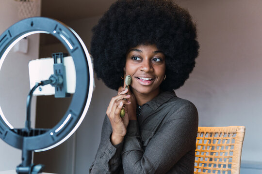 Happy black woman using jade roller while recording vlog