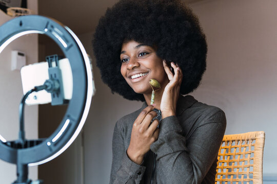 Happy black woman using jade roller while recording vlog