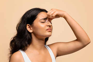 Nosebleeds concept. Young indian woman with closed eyes touching nose bridge