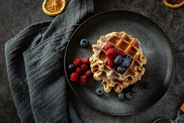 Belgian waffles with blueberries and raspberries on grey plate and dark background