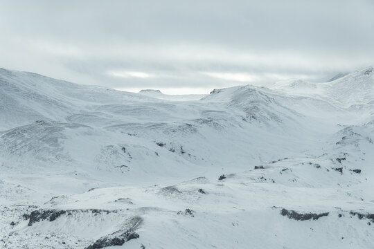 Aerial view of Snowy Mountain Expanse under Cloudy Sky