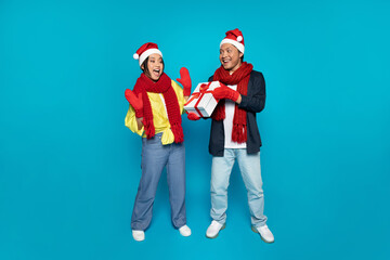 Glad young korean man in hat give present to shocked woman, enjoy winter holidays