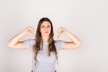 Fototapeta premium Blonde woman looking at camera with two thumbs down on white studio background. Concept of disapproval