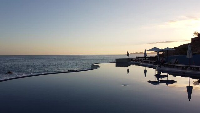 Beautiful shot of a pool overlooking the sea, with people walking on the sandy beach at the sunset