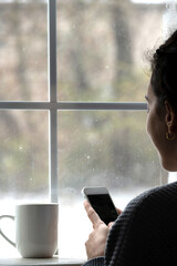 woman with smartphone in front of window with snow