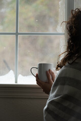 unrecognizable woman holding coffee in front of window with snow