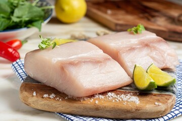 Raw sea common dolphinfish loin, on a wooden board, with lemon, salt and herbs
