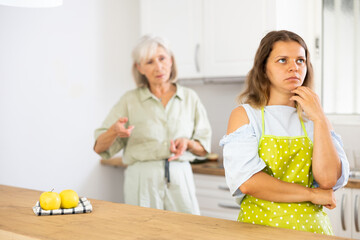 Sad woman ignoring her old mother standing in background and arguing with her.