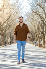 Attractive man on the street walking towards the camera. Handsome bearded man in sweater walking down the street