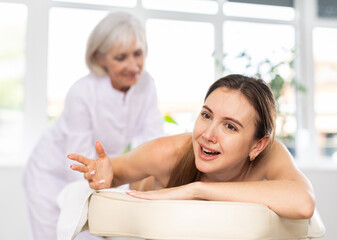 Young female client dissatisfied with work of masseuse in spa salon