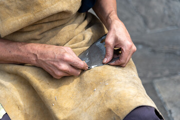 Close-up detail of a blacksmith's hands resting on his brown leather apron, finishing an iron work...