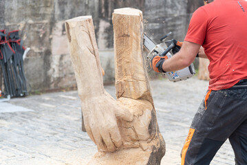 Close-up of a man dressed in work clothes making a wooden sculpture by carving a log with a chainsaw