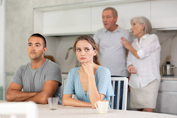 Portrait of an offended married couple in a home kitchen, which mature family members reprimand. Family conflict