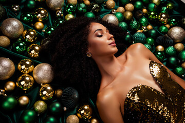 Portrait of stunning party lady lying on emerald silky texture covered decorated with xmas tree glitter baubles