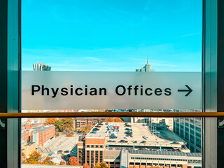 Transparent signage with arrow directing visitors to Physician Offices. Sign affixed to a window overlooking an urban scene.