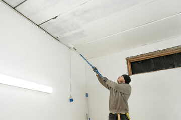 Skilled Worker in Work Attire Paints Interior with Precision Using Roller.