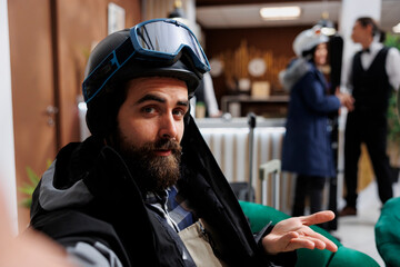 Tourist dressed in snow gear and holding smartphone, captures his adventure at ski resort. Taking a selfie in hotel lobby, male guest documents the excitement of snowboarding and skiing activities.