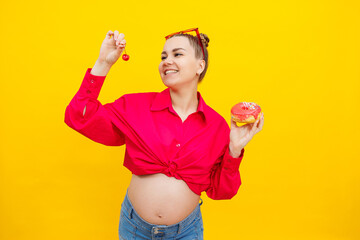 A bright pregnant woman in a pink shirt on a yellow background eats sweets. Sweet donuts in the hands of a pregnant woman.