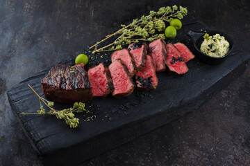 Barbecue dry aged angus roast beef steak with herb butter and dried oregano served as close-up on a rustic charred cutting board with copy space