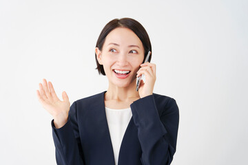 スマートフォンで電話をしながら笑顔で驚く中年のビジネスウーマン　白背景