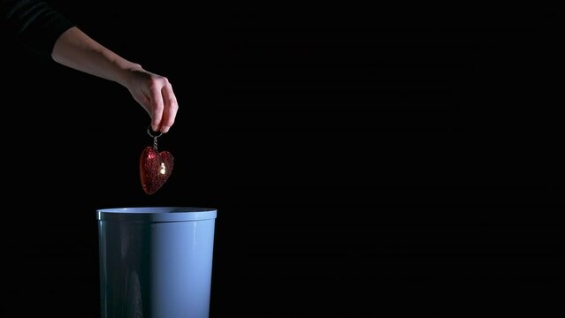 Throw heart into trash bin. A woman with broken love throw the heart symbol into bin on the black background.