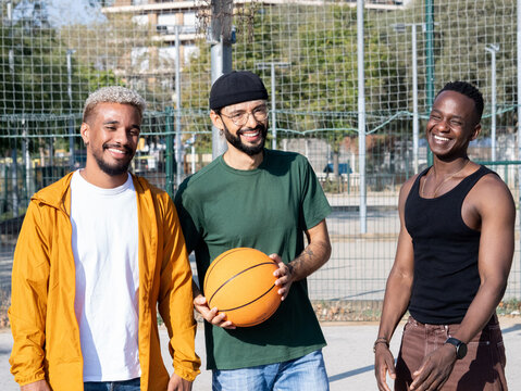 Portrait of three diverse young men lookingsmiling at camera on a basketball court with a ball in their hand 
