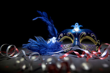 Festive blue and gold venetian carnival mask with streamers and confetti on a black background