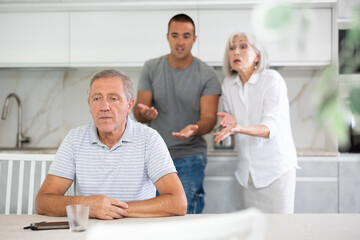 Elderly woman and adult man during family quarrel with elderly man in kitchen