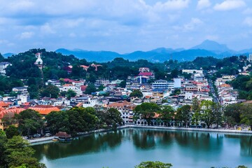 Aerial view of Kandy Lake surrounded by green mountains and building in Sri Lanka on a cloudy day