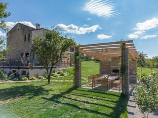 Wide shot of a wood and stone building next to a wooden pergola in a garden.