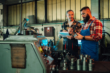 Two metal turners by a lathe machine in a factory, measuring a cylinder.