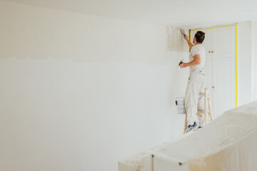 A plasterer on ladder skim coating and plastering walls.