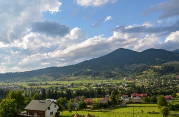 Picturesque view of the Carpathian mountain village Verkhovyna in the valley and green mountain slopes covered forest and grassy meadows on background