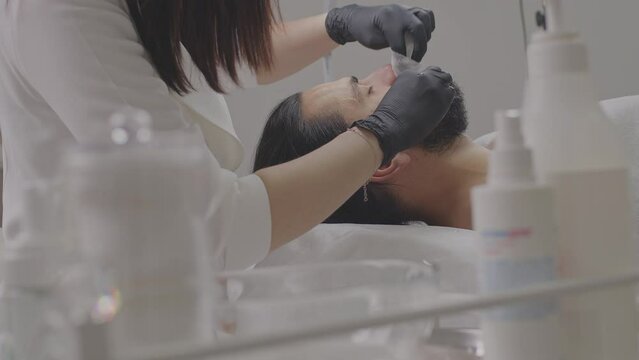 Closeup of young man face. Facial massage with scrub. Beautician hands in gloves
