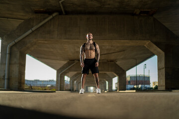 Chico joven tatuado y musculoso posando y haciendo deporte en la calle en un tunel con un puente de...